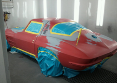 A red car is being painted in a paint booth