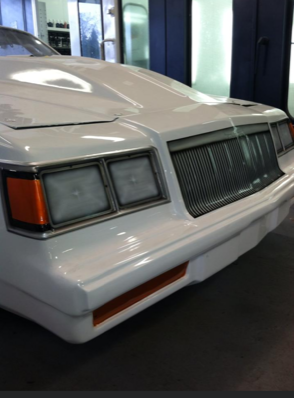 A white car is parked in a garage with the hood up