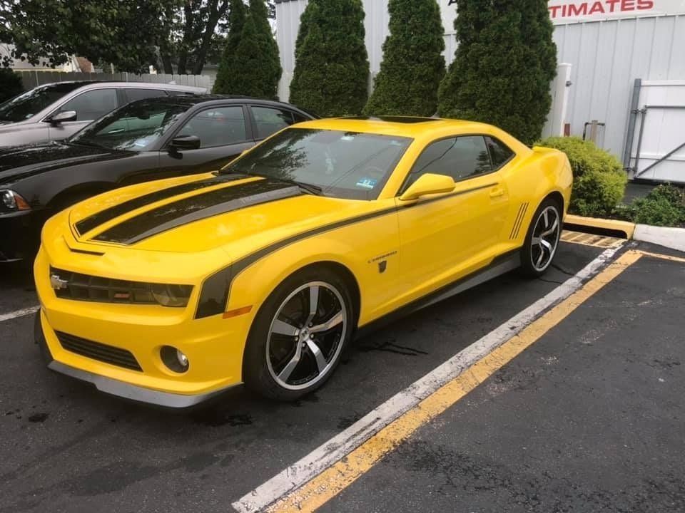 A yellow car with black stripes is parked in a parking lot.