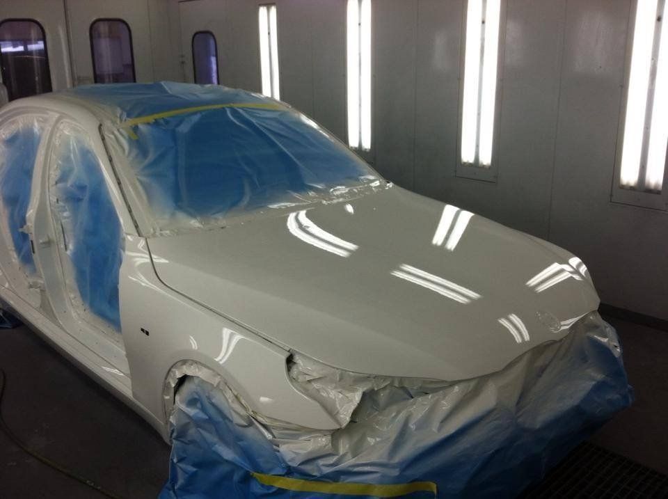 A white car is being painted in a paint booth