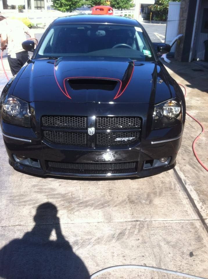 A black car with a red stripe on the hood is parked in a parking lot.