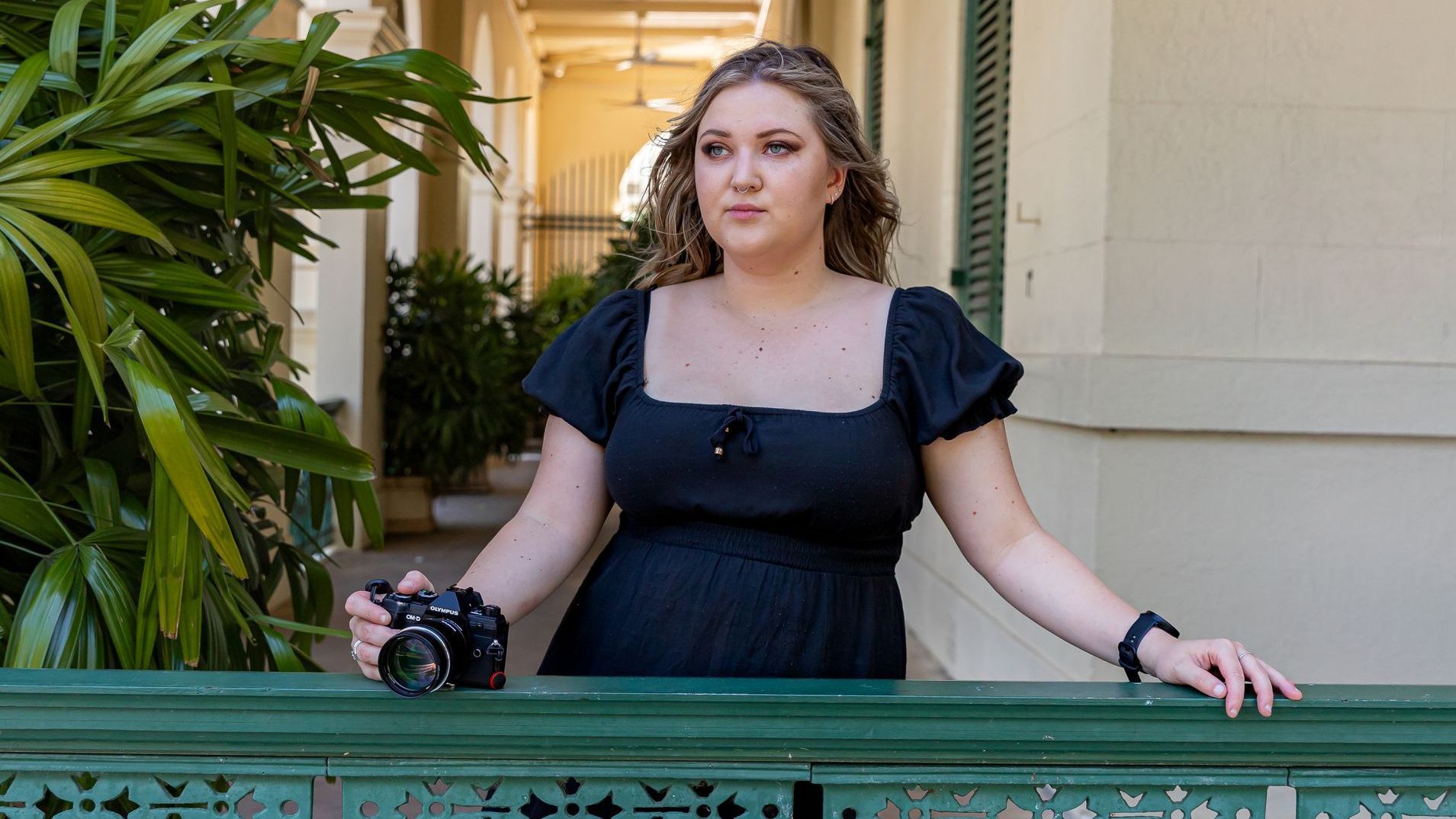 A woman in a black dress is standing on a balcony holding a camera.