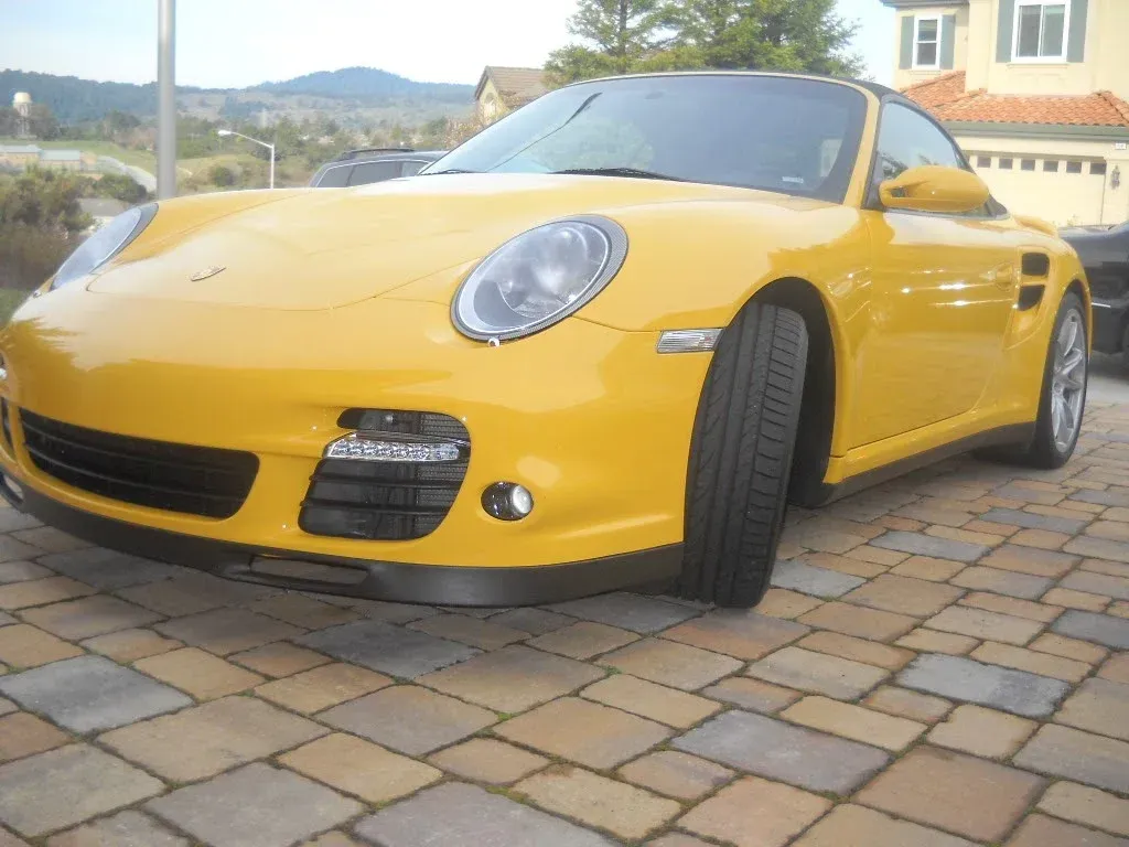 Yellow Porsche sports car parked on brick pavers in front of a house.