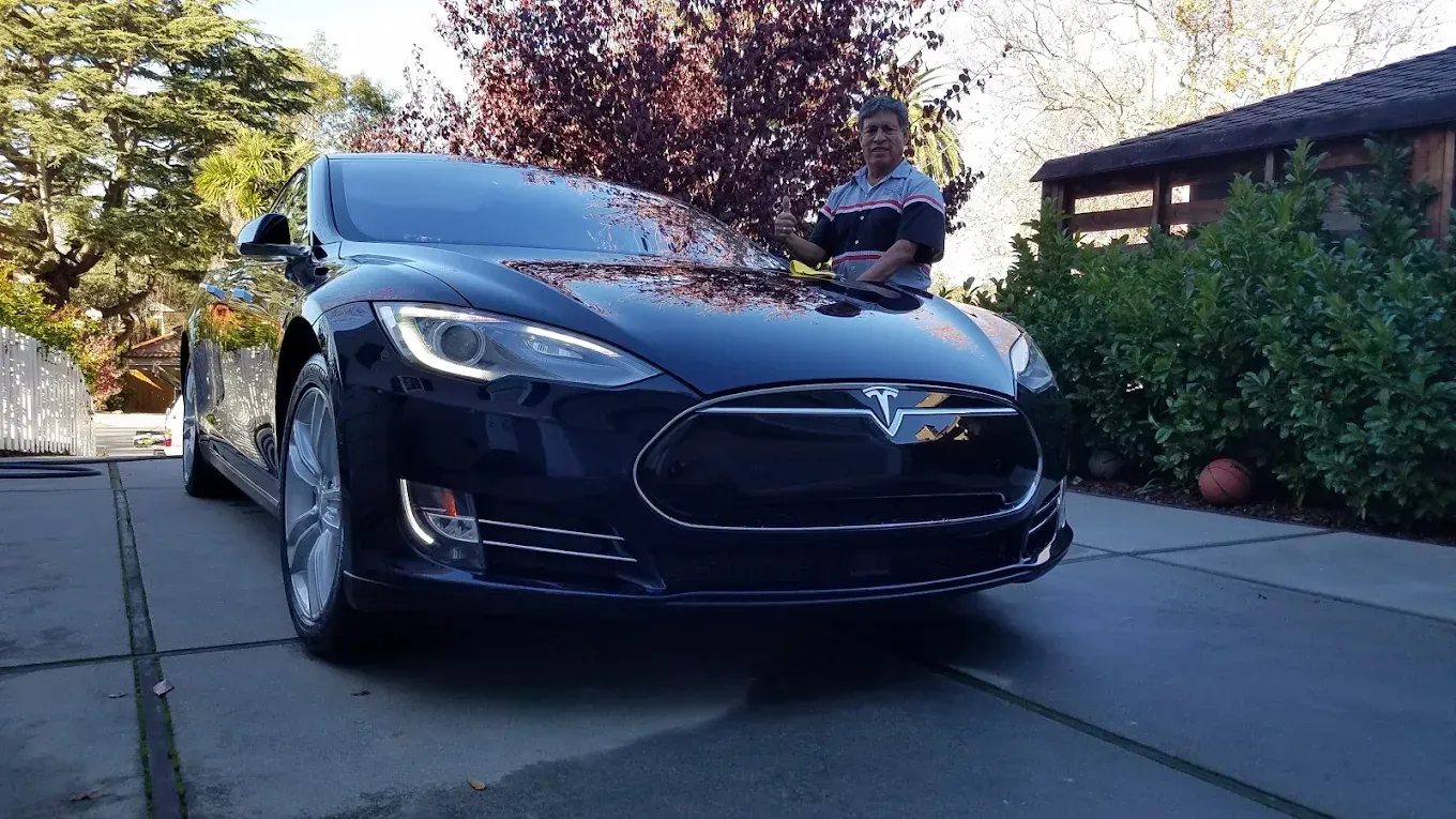 Man cleaning a dark blue Tesla car parked in a driveway.