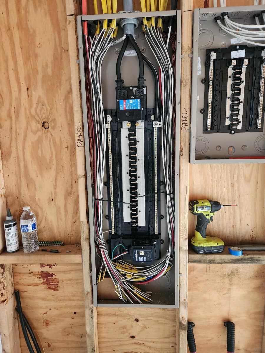 Electrician kneeling by a wall panel, wiring a breaker box in a bright room.