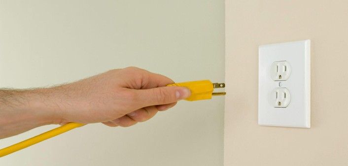 A hand plugging a yellow power cord into a wall outlet