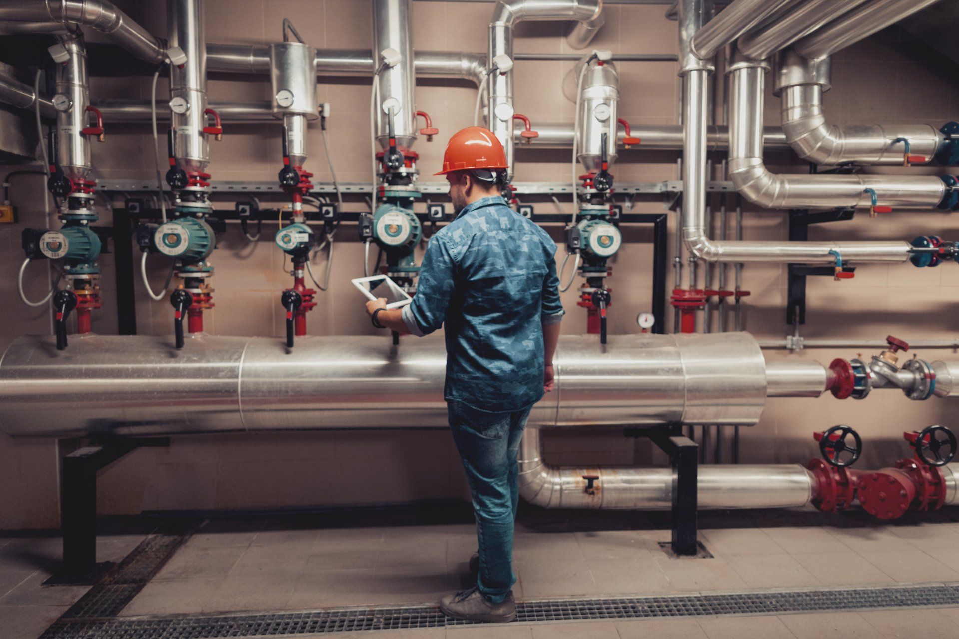Gas Heater — Springville, UT — Blue Plumbing and Drain Cleaning A man is standing in a room with pipes and looking at a tablet.