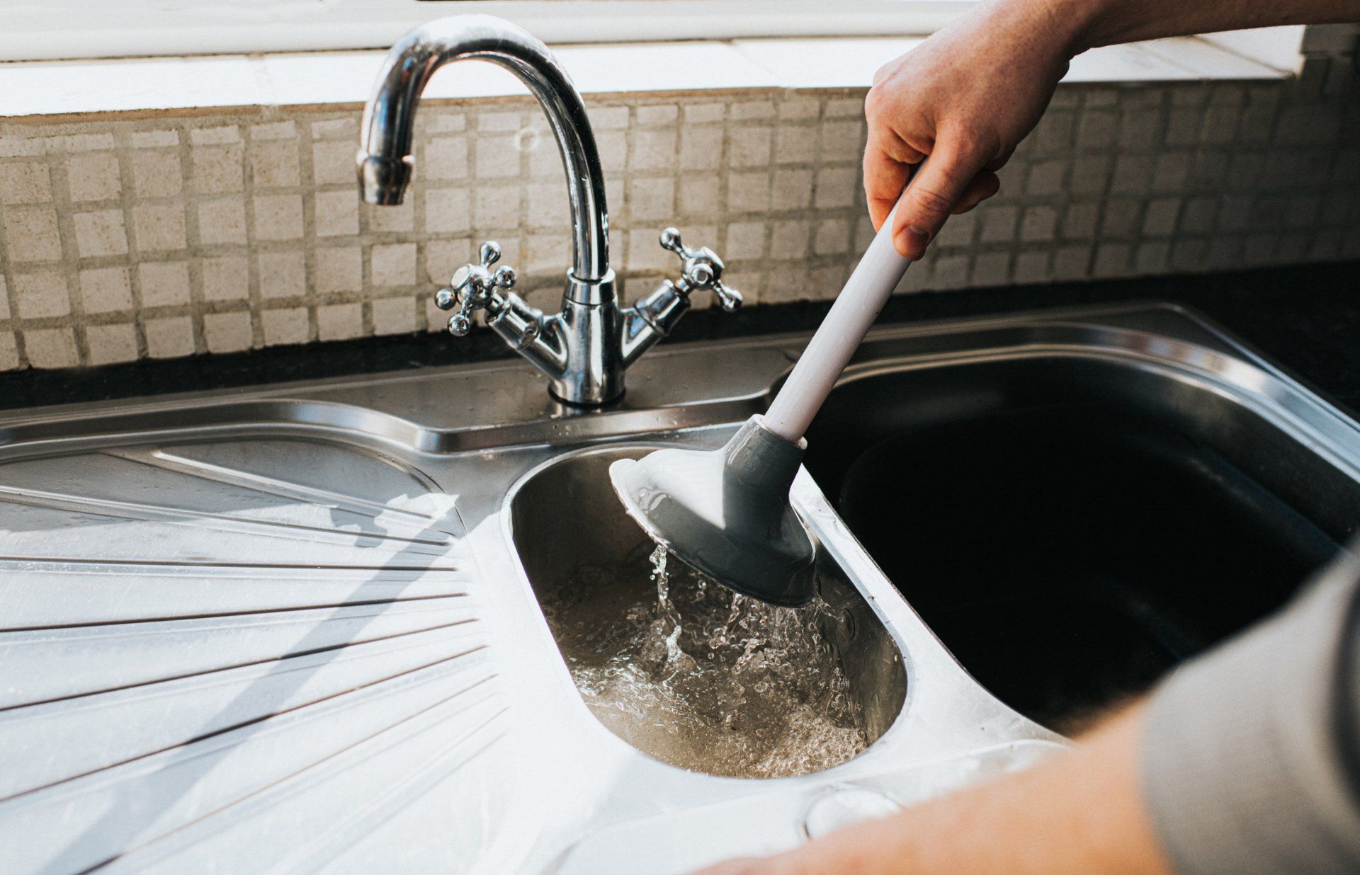 A person is cleaning a sink with a plunger.