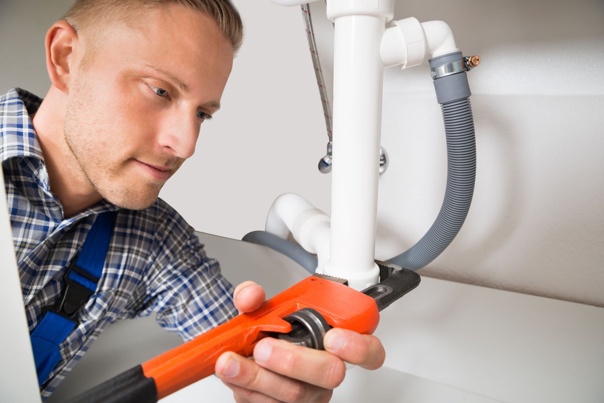 Close-up of a male plumber repairing a sink pipe with an adjustable wrench.