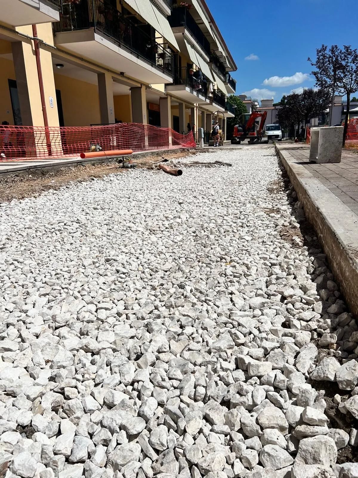 Un cantiere edile ricoperto di ghiaia di fronte a un moderno condominio, sotto un cielo azzurro brillante.