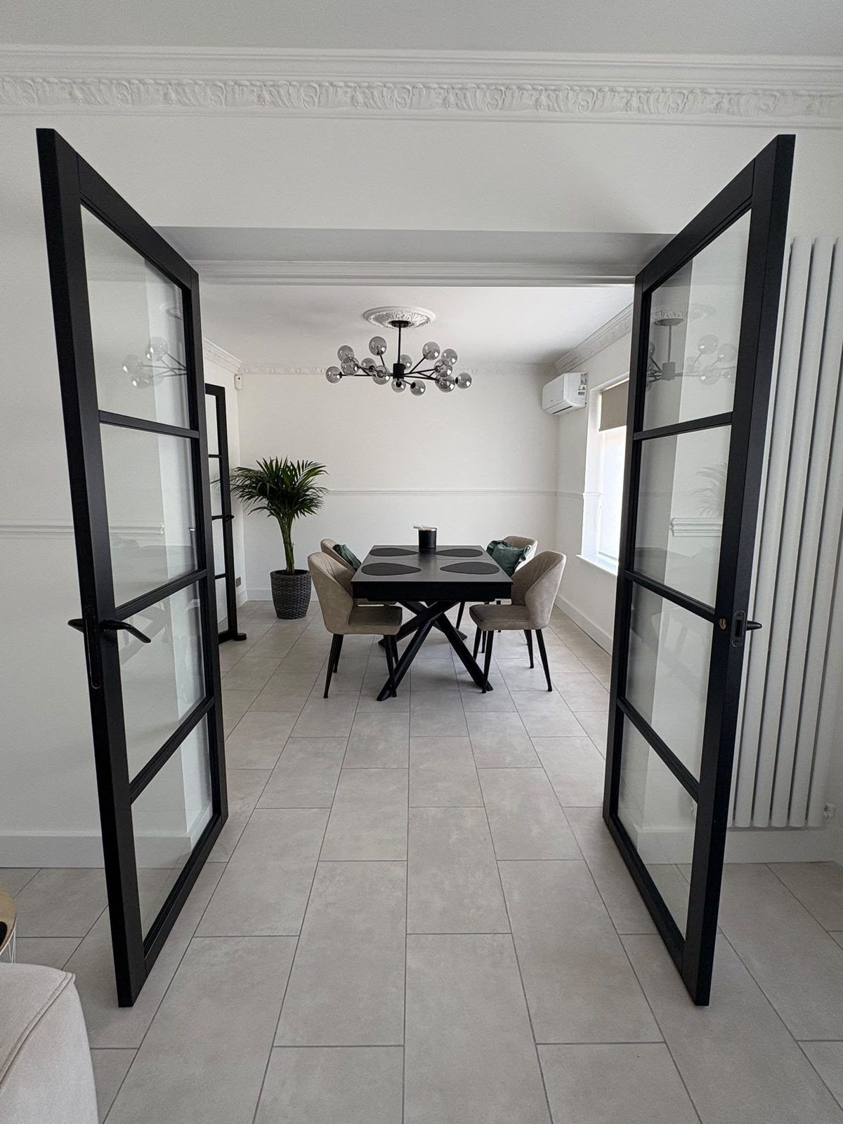 Black-framed glazed double doors opening into a dining room with coving and a ceiling rose