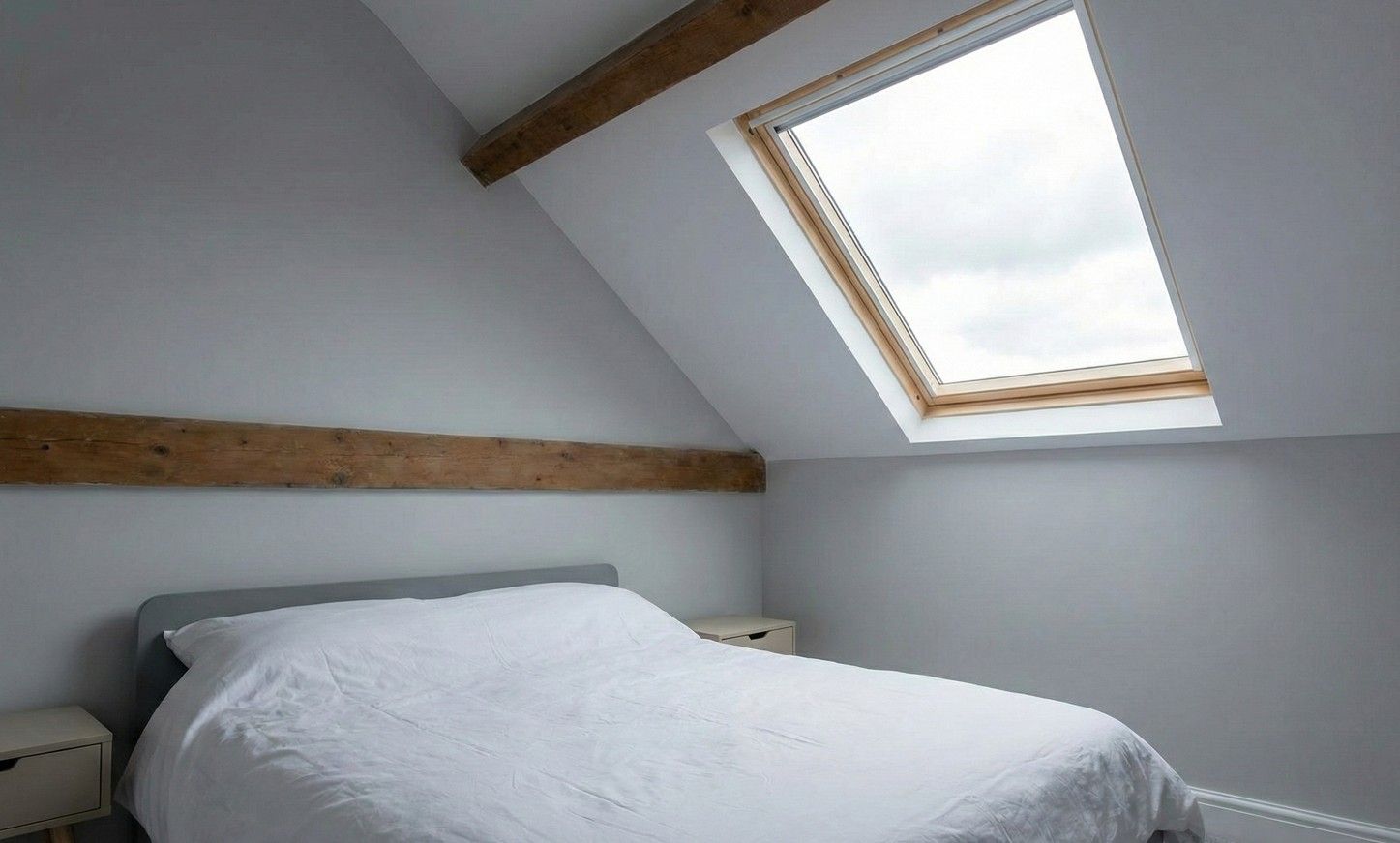Loft bedroom with a double bed under a rooflight and pale grey sloping walls