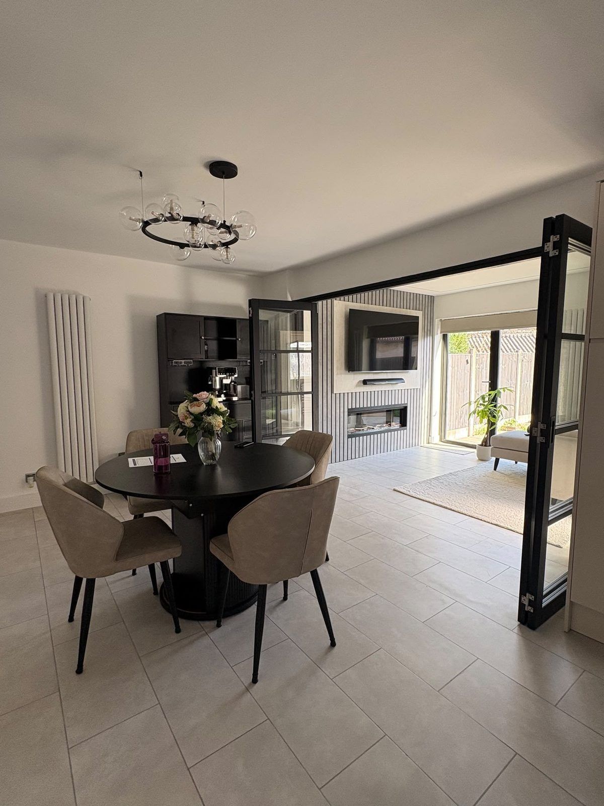 Open-plan dining area with a globe chandelier and internal bifold doors folded back to the lounge