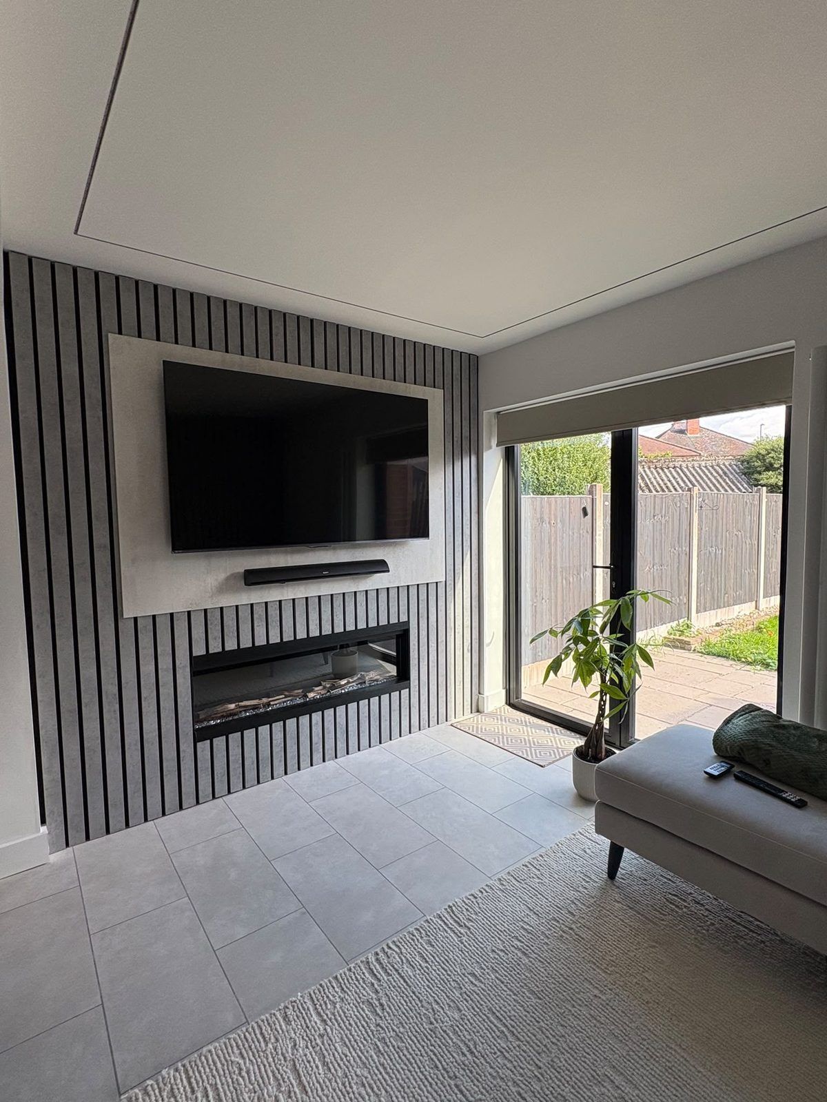Slatted panel media wall with a wall-mounted TV, soundbar and inset electric fire beside patio doors