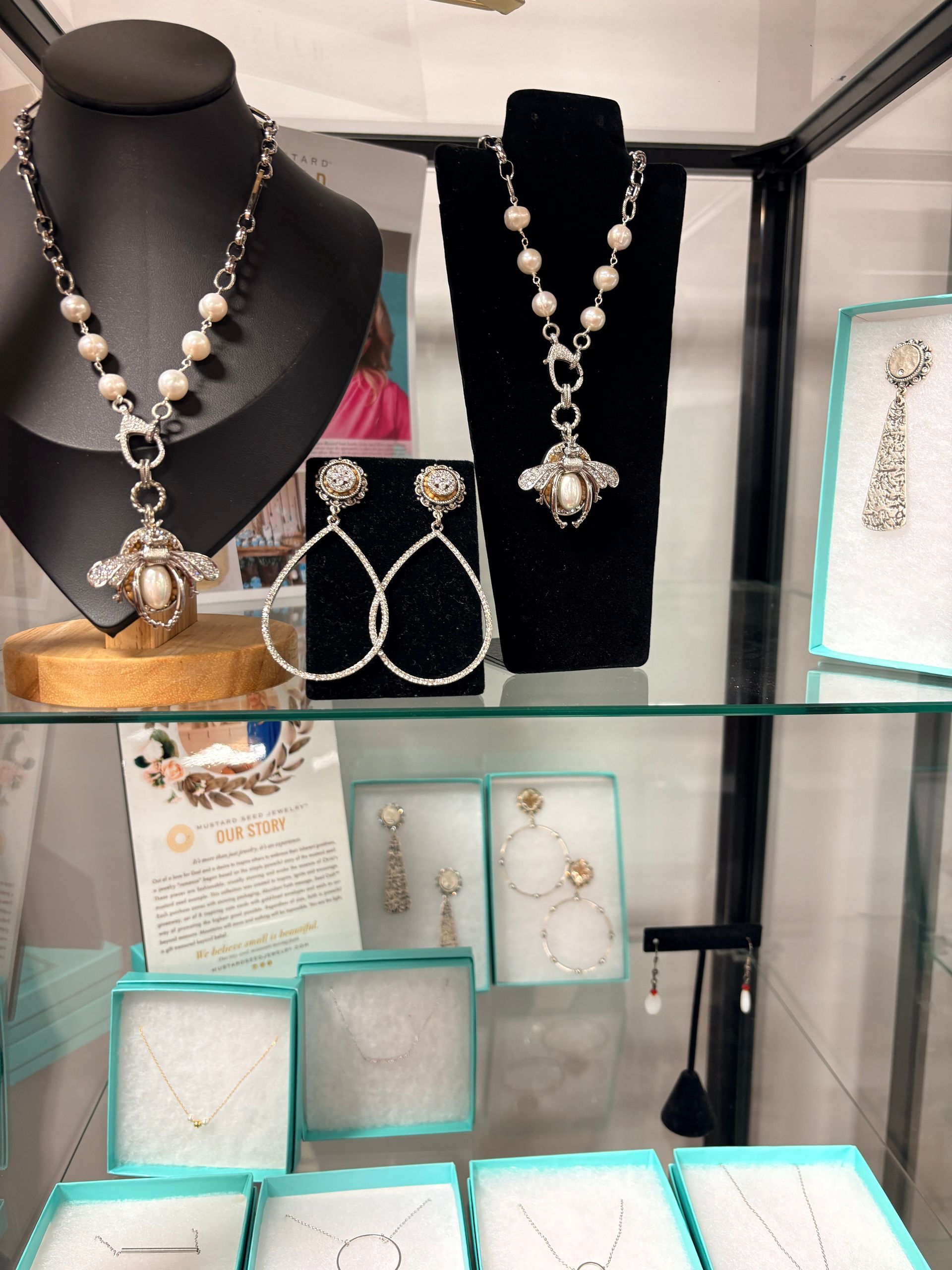 Jewelry display with necklaces, earrings, and rings on black and white bust stands in a glass case