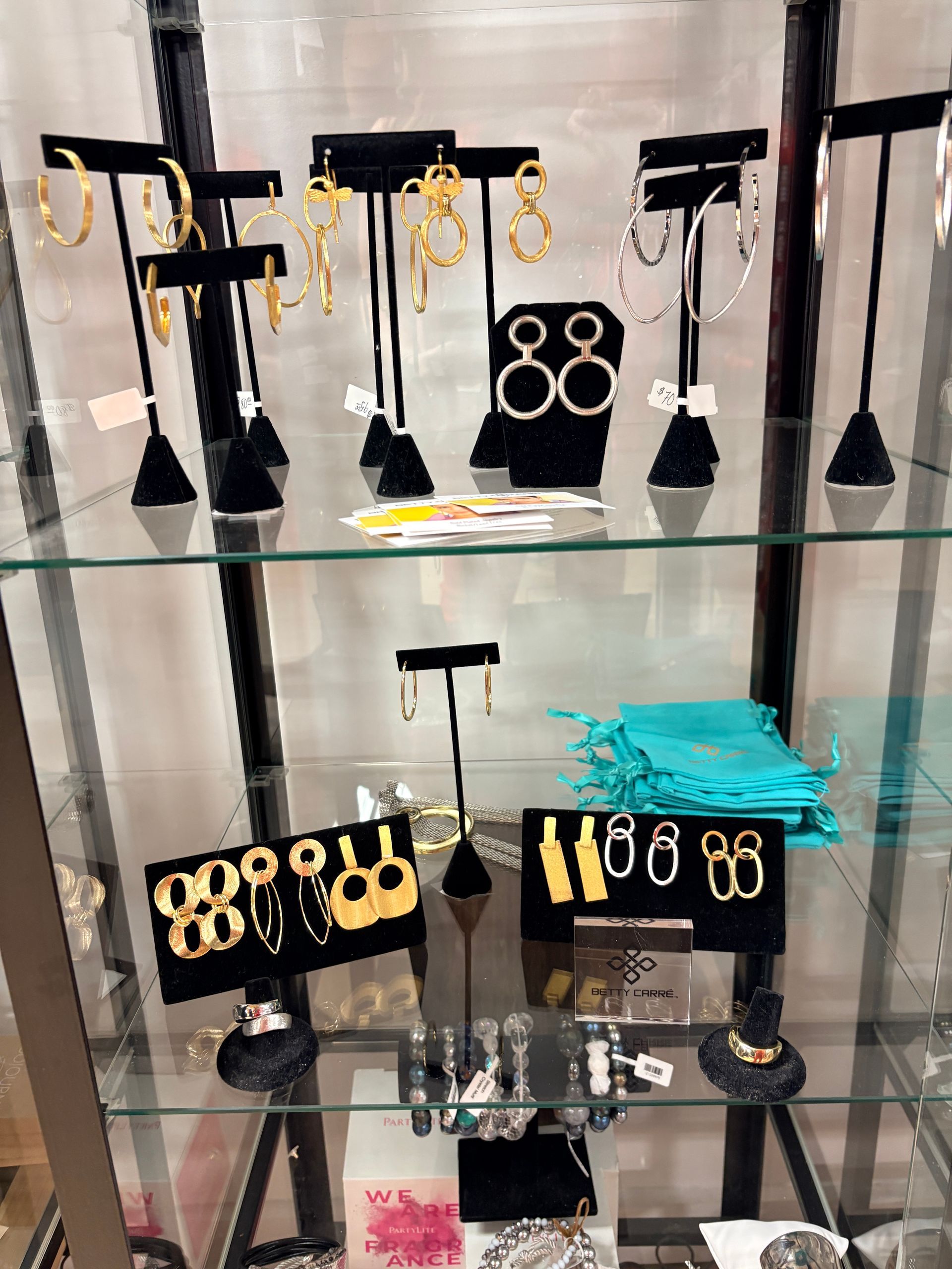 Glass display case with black and gold earrings on stands, plus a turquoise pouch on the middle shelf