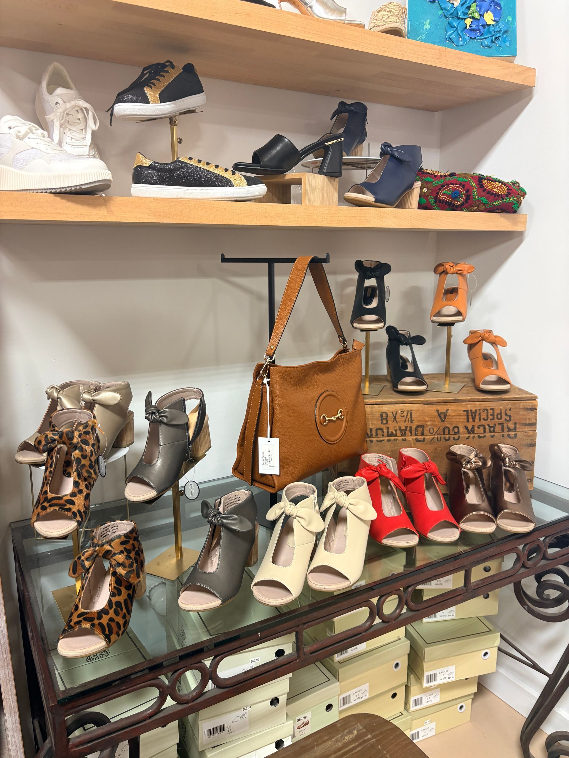 Shoe display on shelves with assorted boots, sandals, handbags, and boxes in a retail shop.