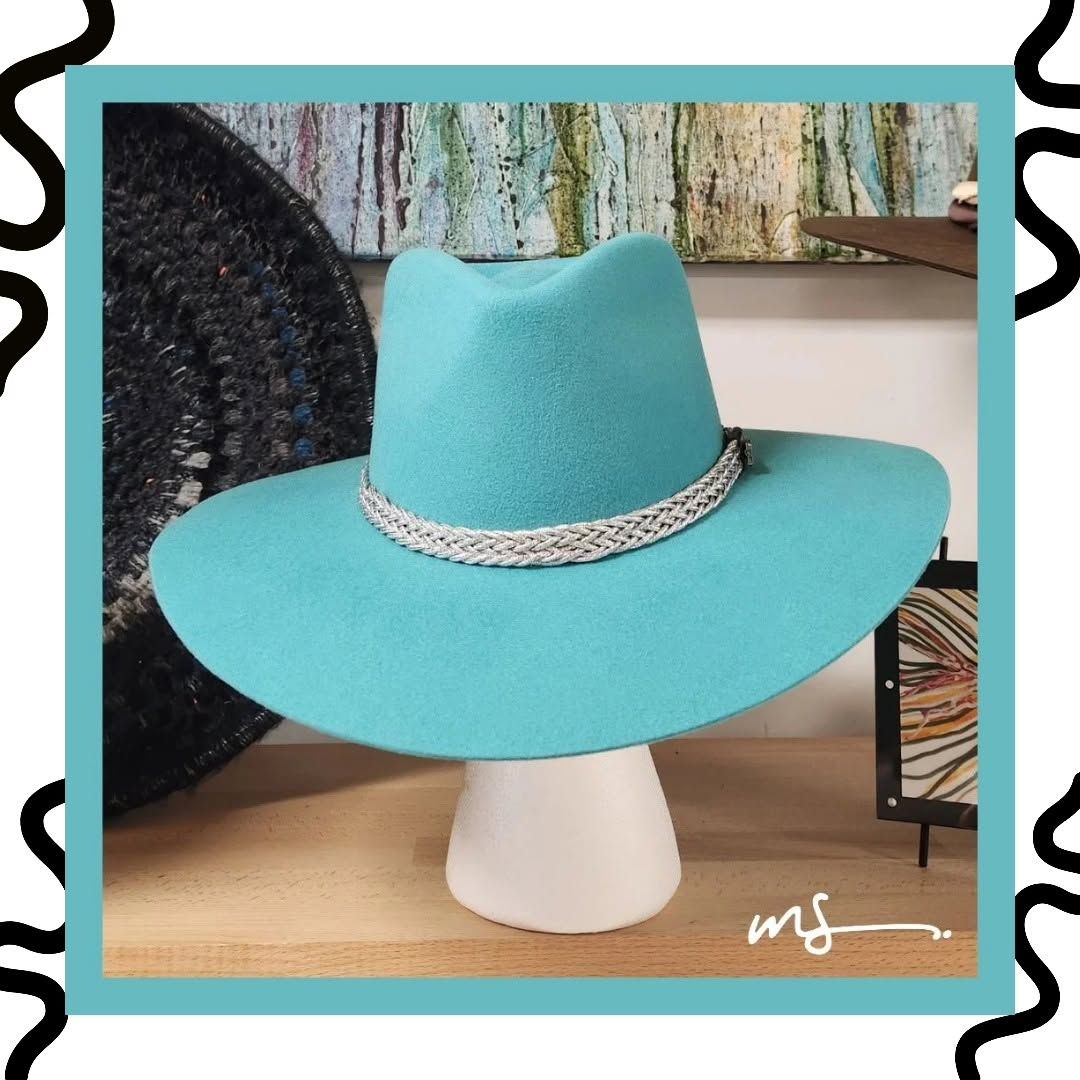 Turquoise cowboy hat with braided band on a white stand indoors