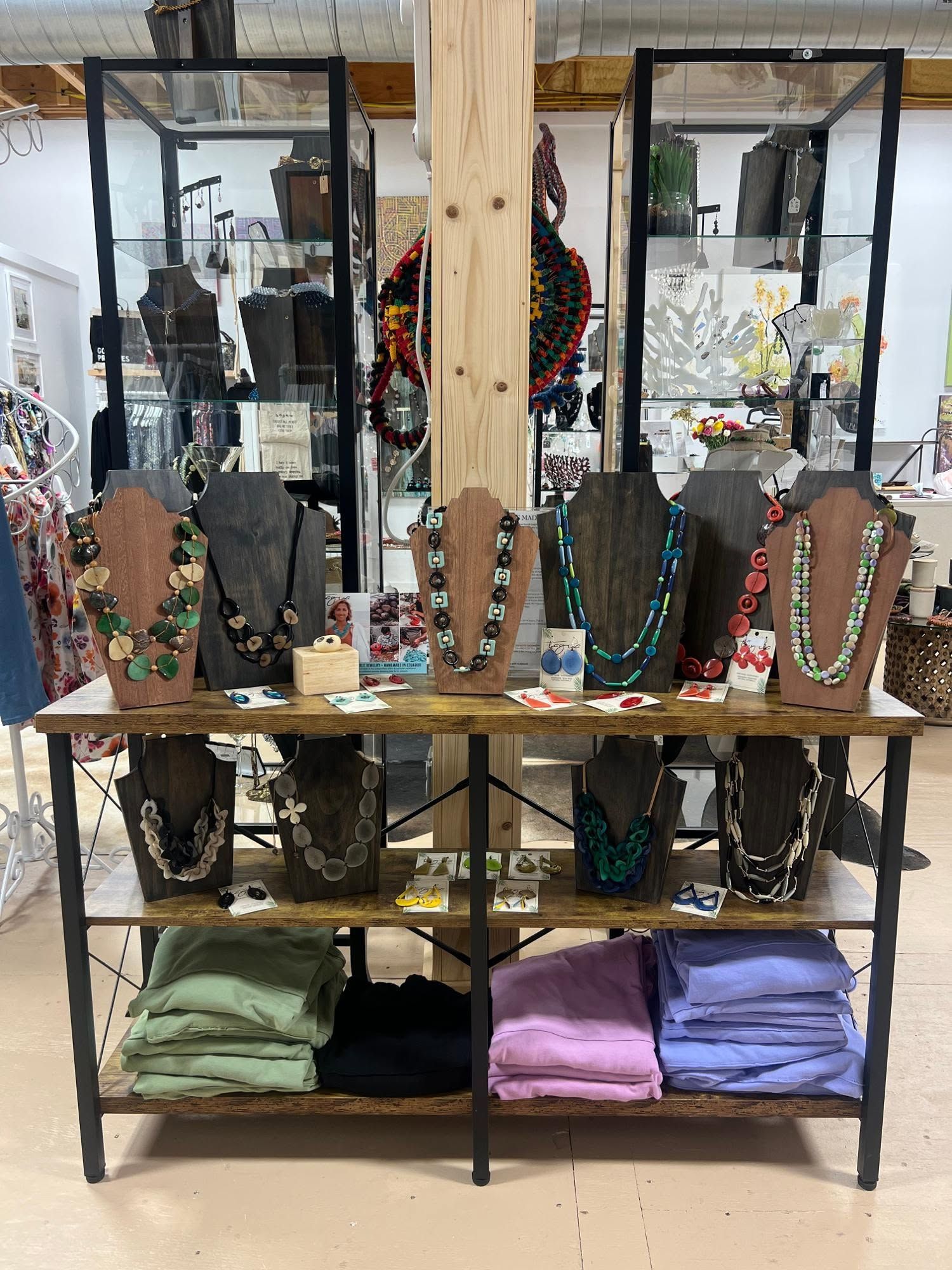 Display of beaded necklaces on shelves with folded shirts below in a market stall