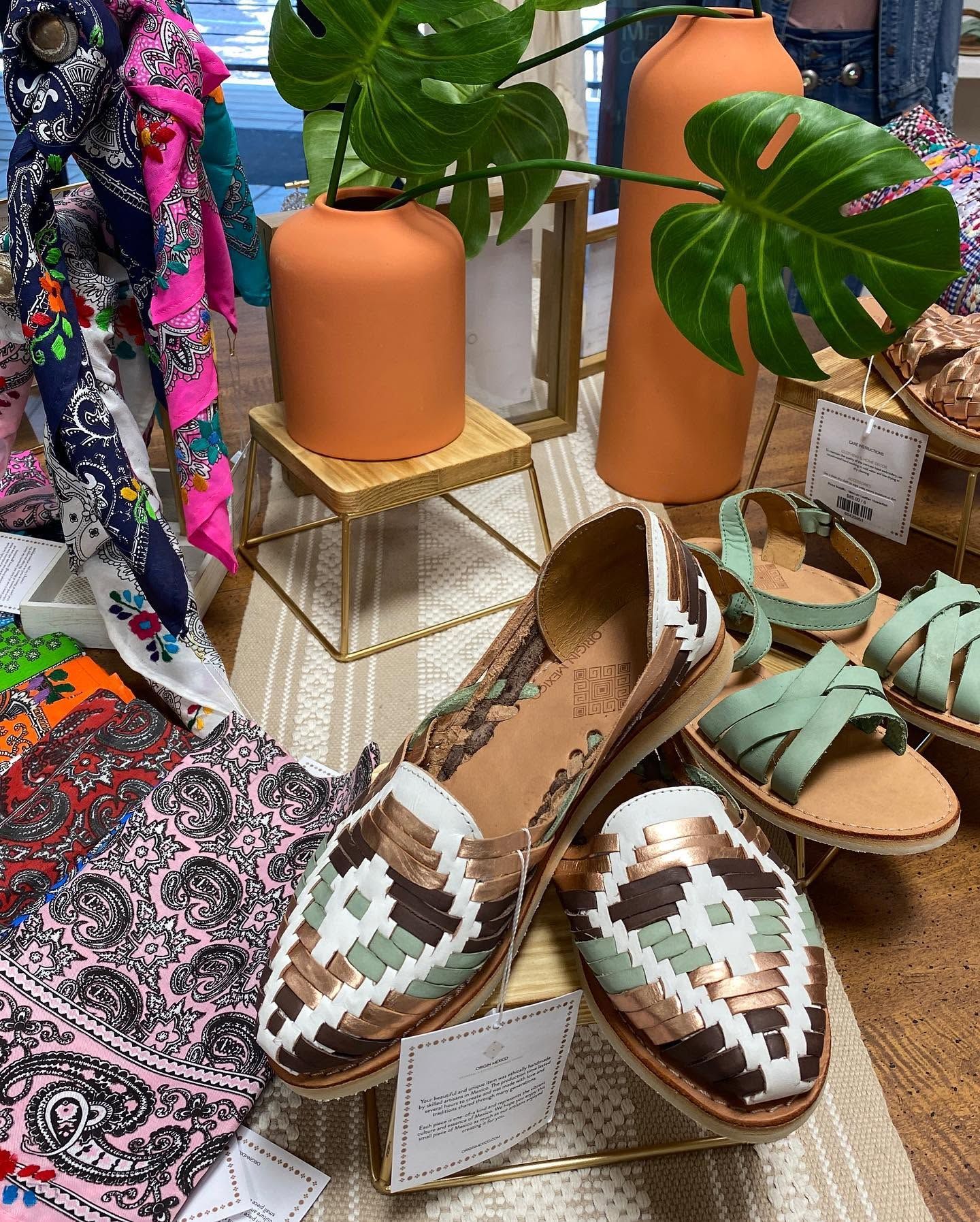 Patterned loafers displayed with sandals, colorful textiles, and potted plants in a boutique setting