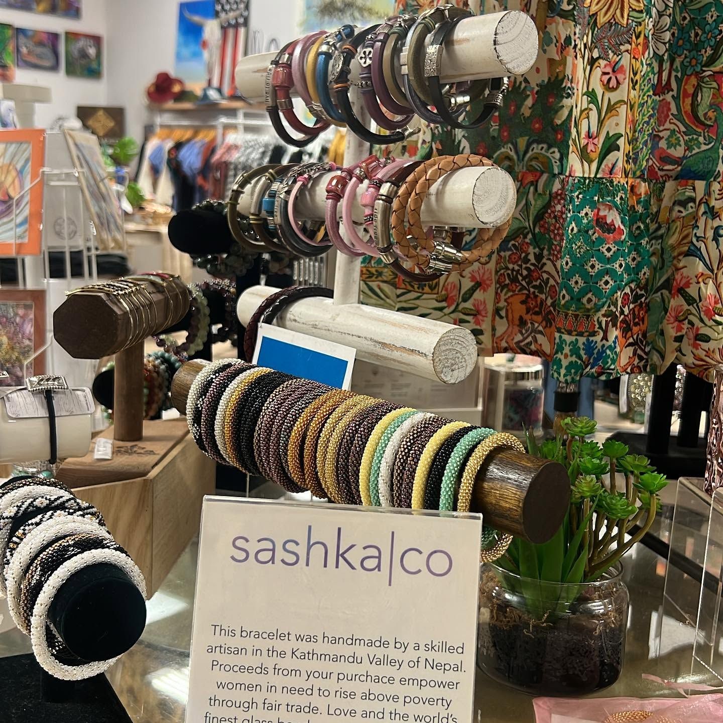 Colorful beaded bracelets displayed on wooden stands at a market stall with a “sashka.co” sign