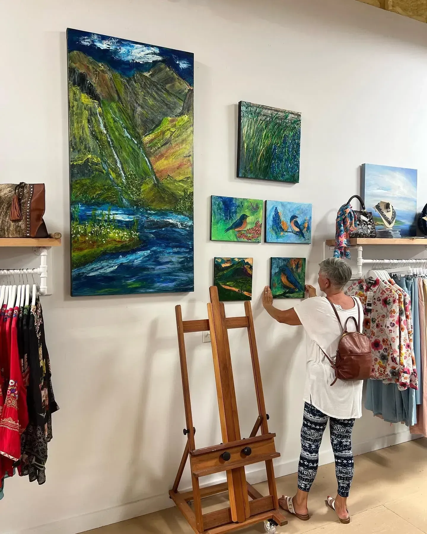 Artist arranging easels in a gallery with colorful landscape paintings on the wall