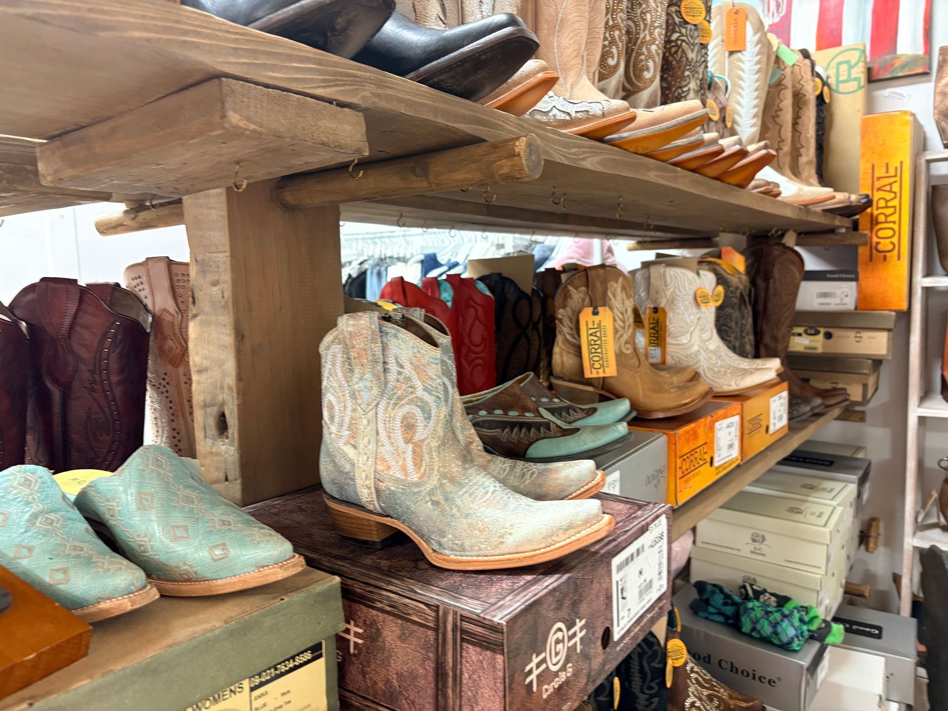 Western boots displayed on wooden shelves in a rustic store, including turquoise and cream pairs