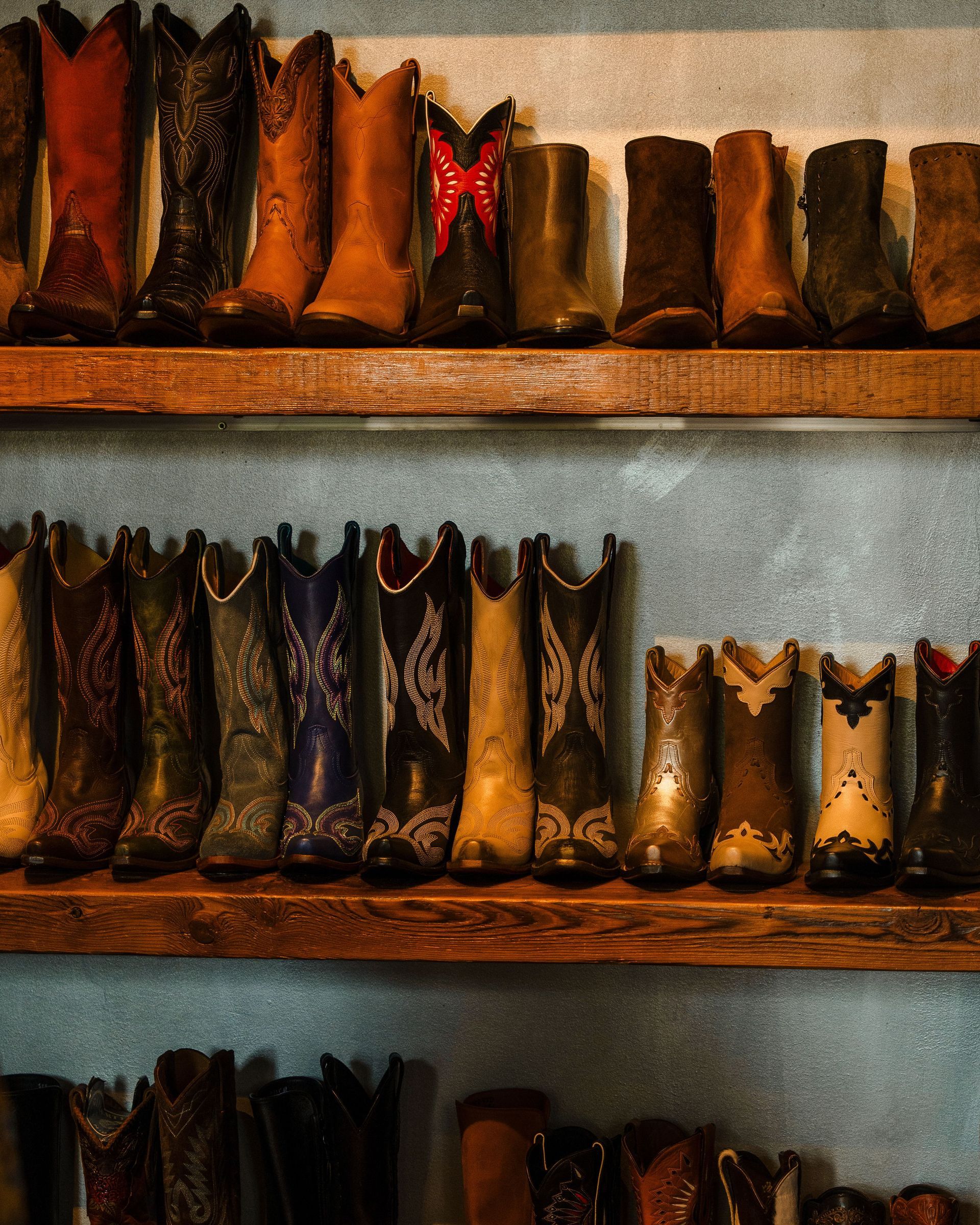 Rows of worn boots and shoes displayed on wooden shelves against a gray wall.