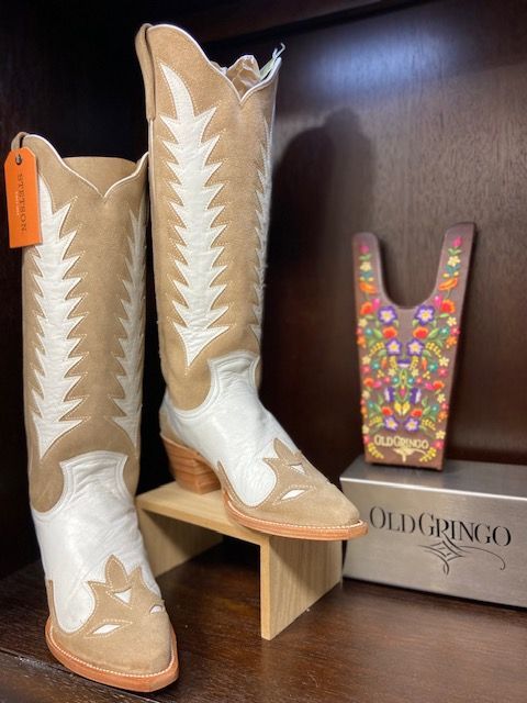 Pair of white-and-tan cowboy boots displayed beside a colorful beaded U-shaped accessory on a wooden box