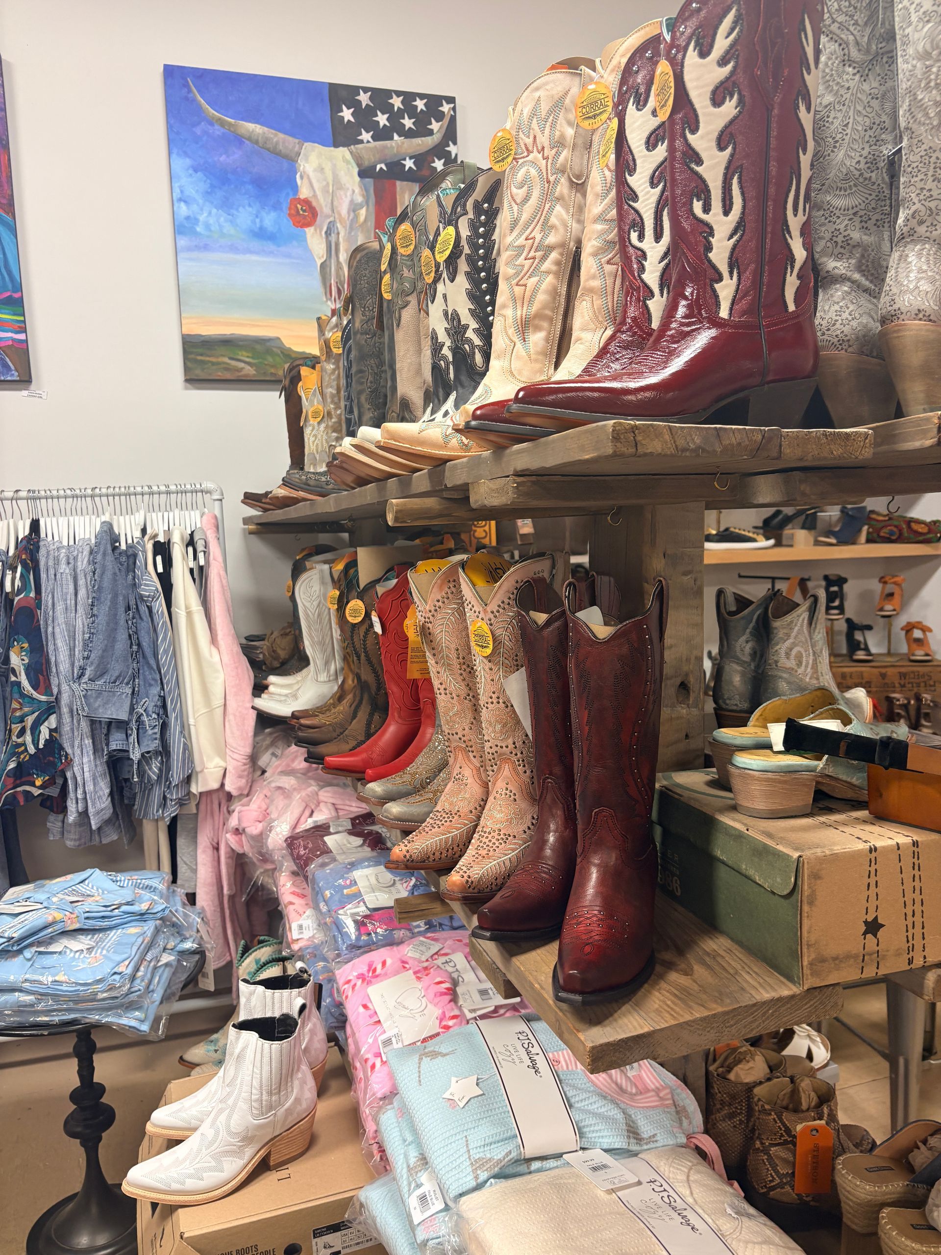 Shelves of colorful cowboy boots in a shop, with patterned textiles and a wall flag in the background