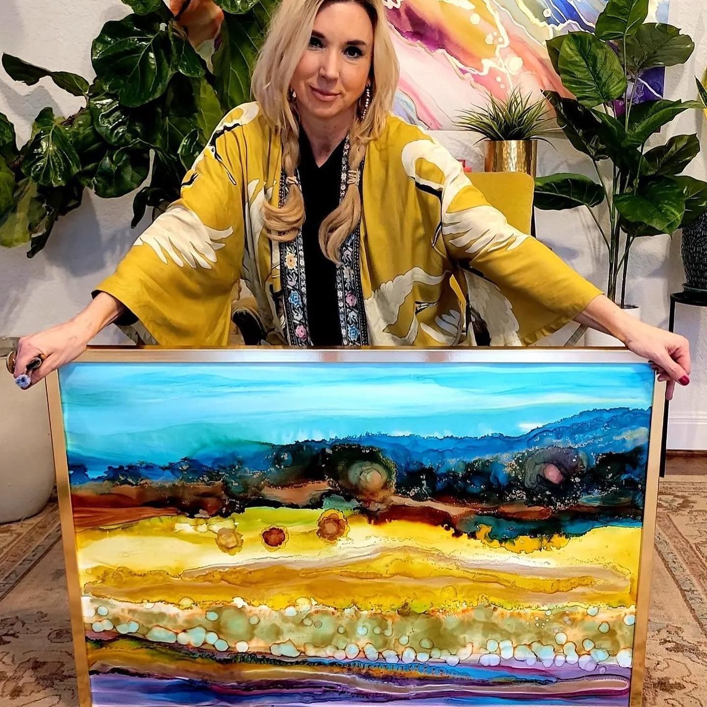 Canvas painting of a green field on an easel, with painting supplies on a table in a studio