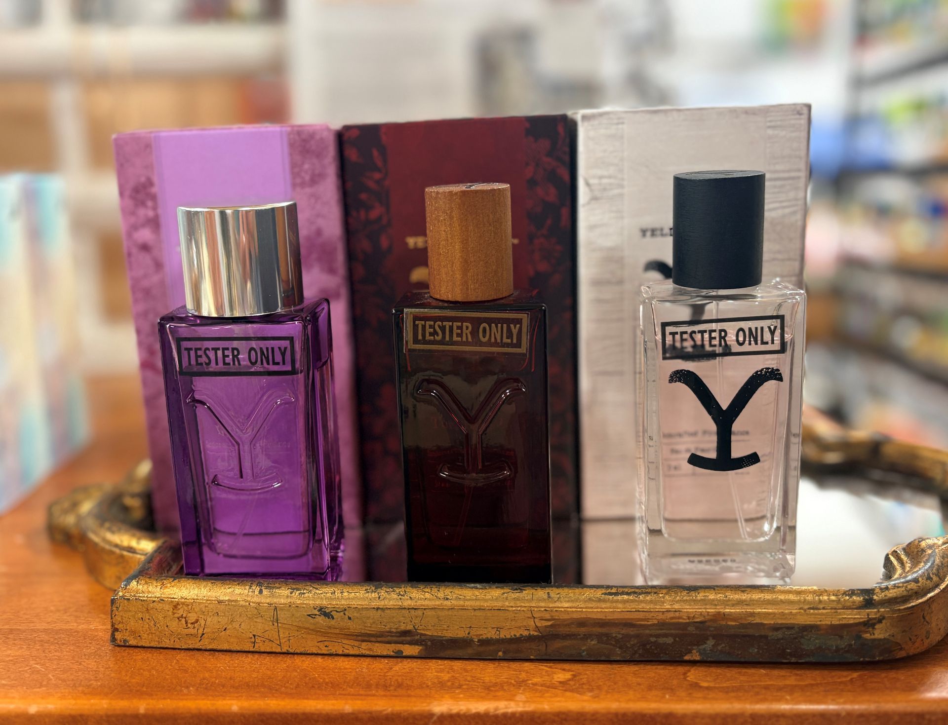 Three perfume bottles on a gold tray: purple, dark red, and clear with a Y label.