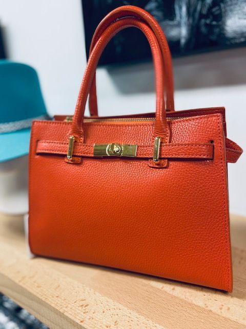 Orange structured handbag with top handles and gold clasp on a tabletop.