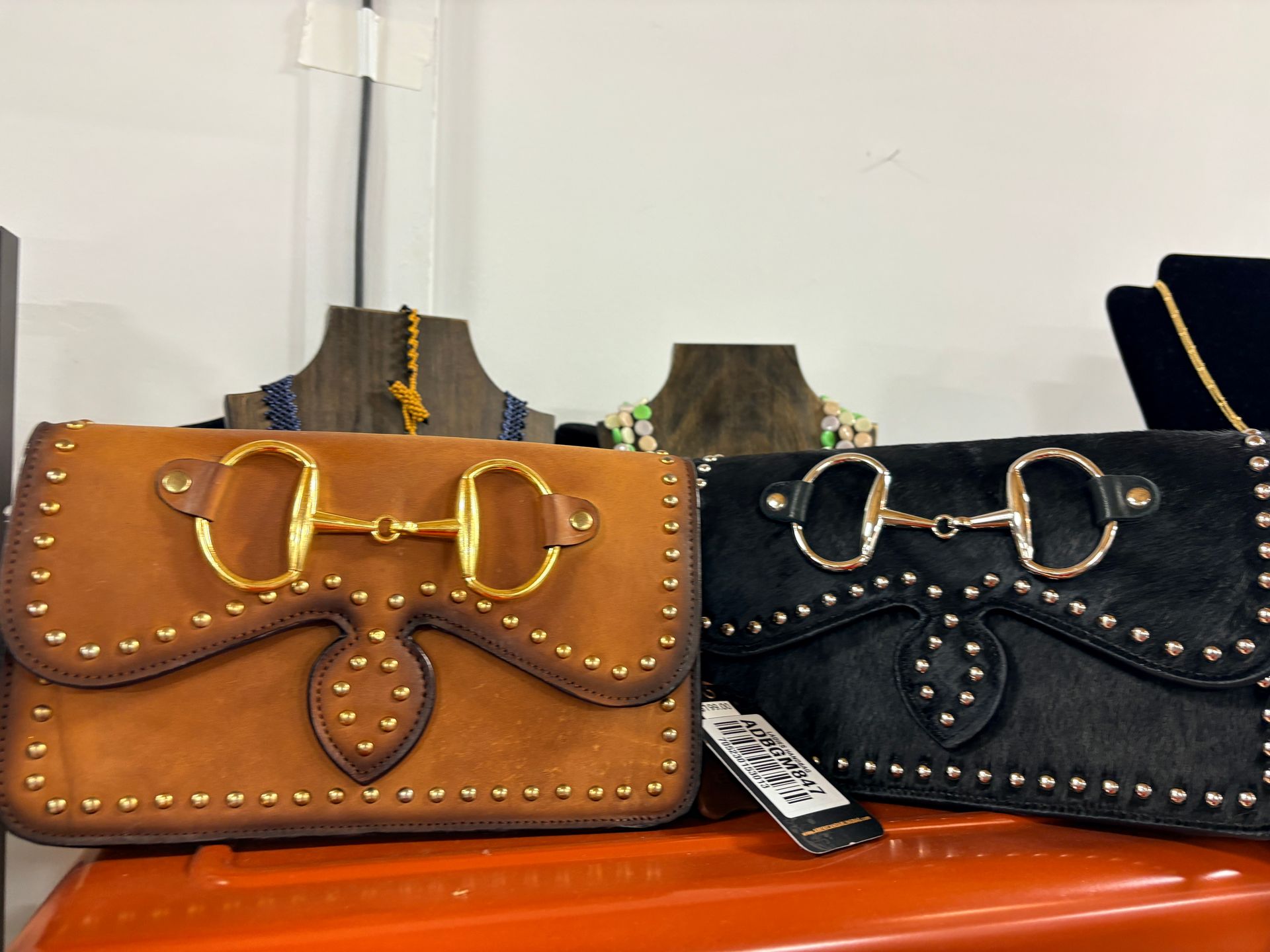 Two leather handbags, tan and black, with gold bows and studded trim on a shelf.