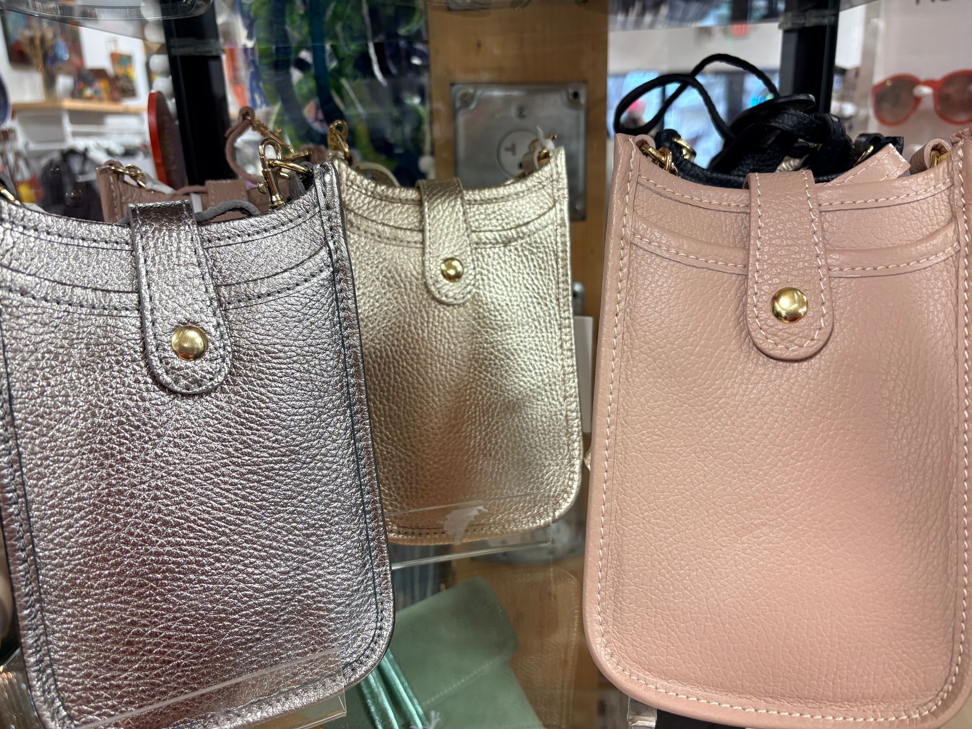 Three glittery handbags in silver, gold, and pink displayed on a store shelf