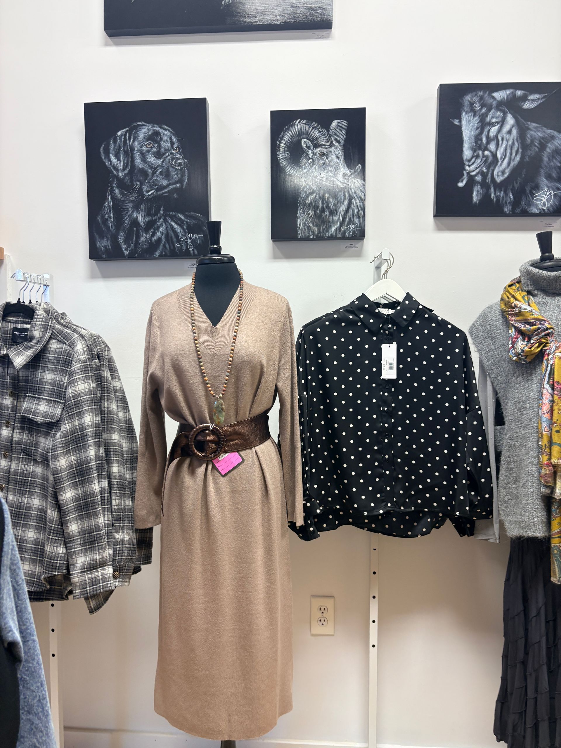 Clothing display with patterned tops and a tan belted dress on mannequins in a boutique window
