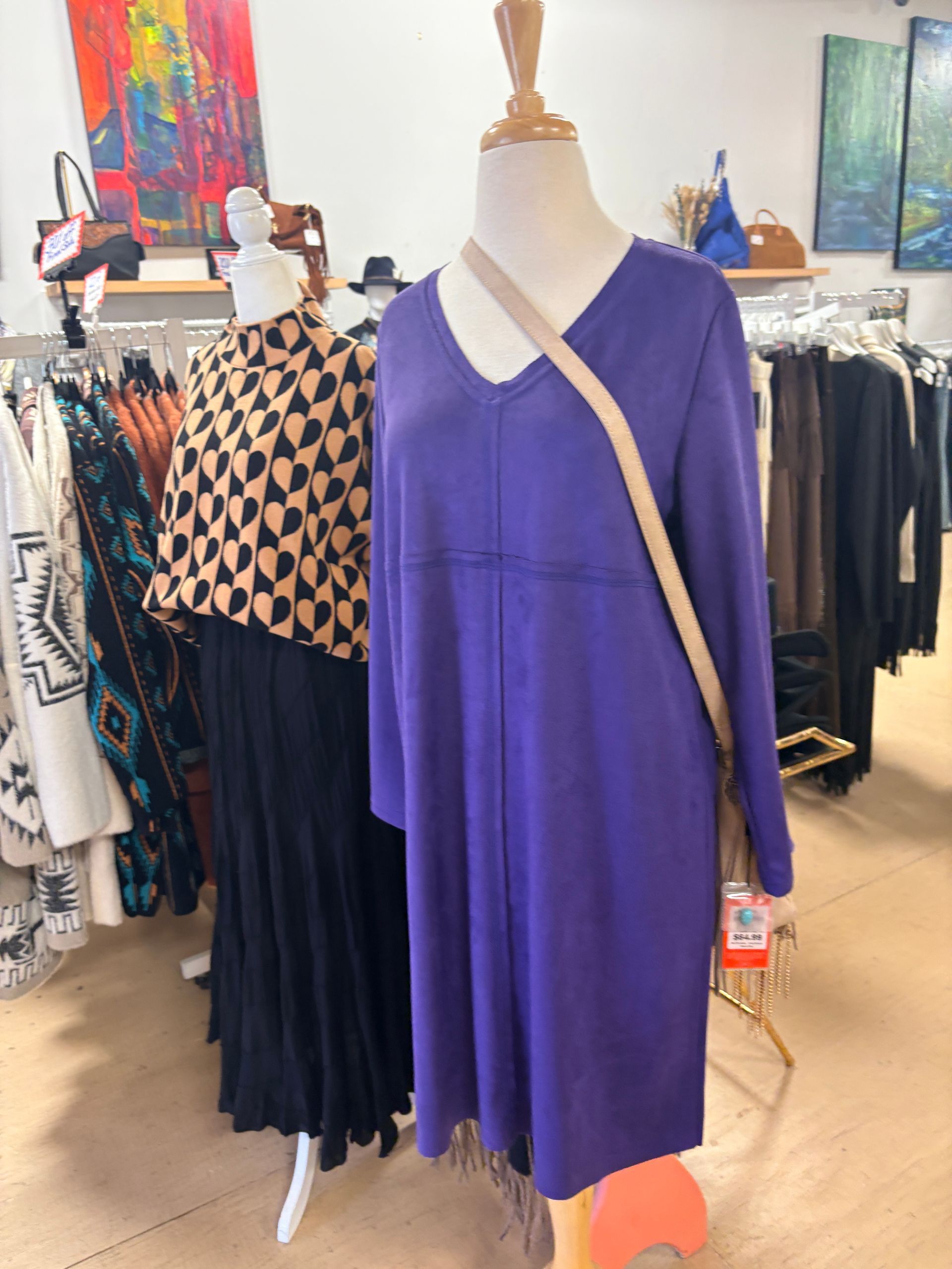 Purple long-sleeve dress on a mannequin in a clothing store, with racks of garments in the background.