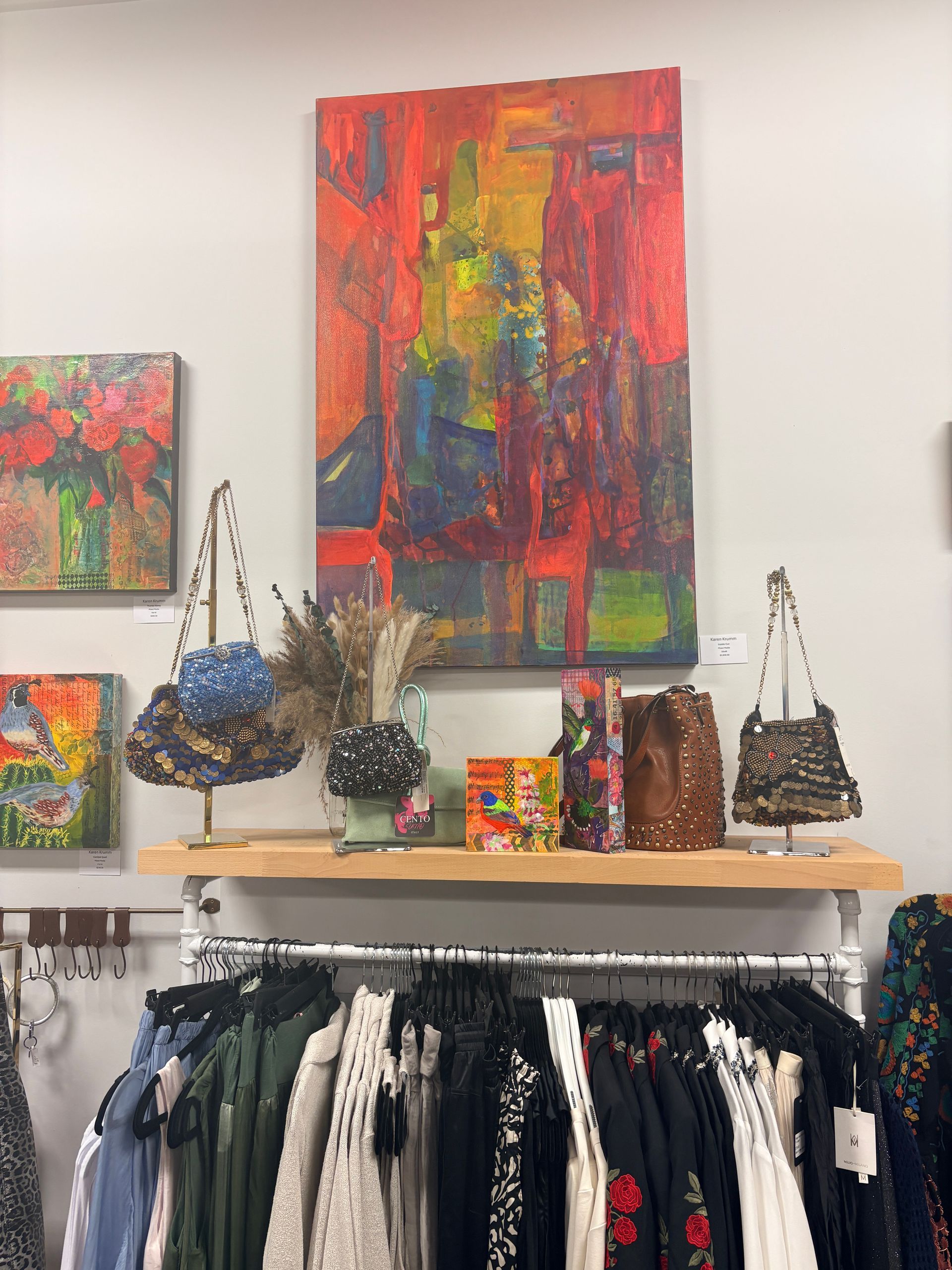 Art gallery wall with colorful abstract paintings, handbags, and a clothing rack below.
