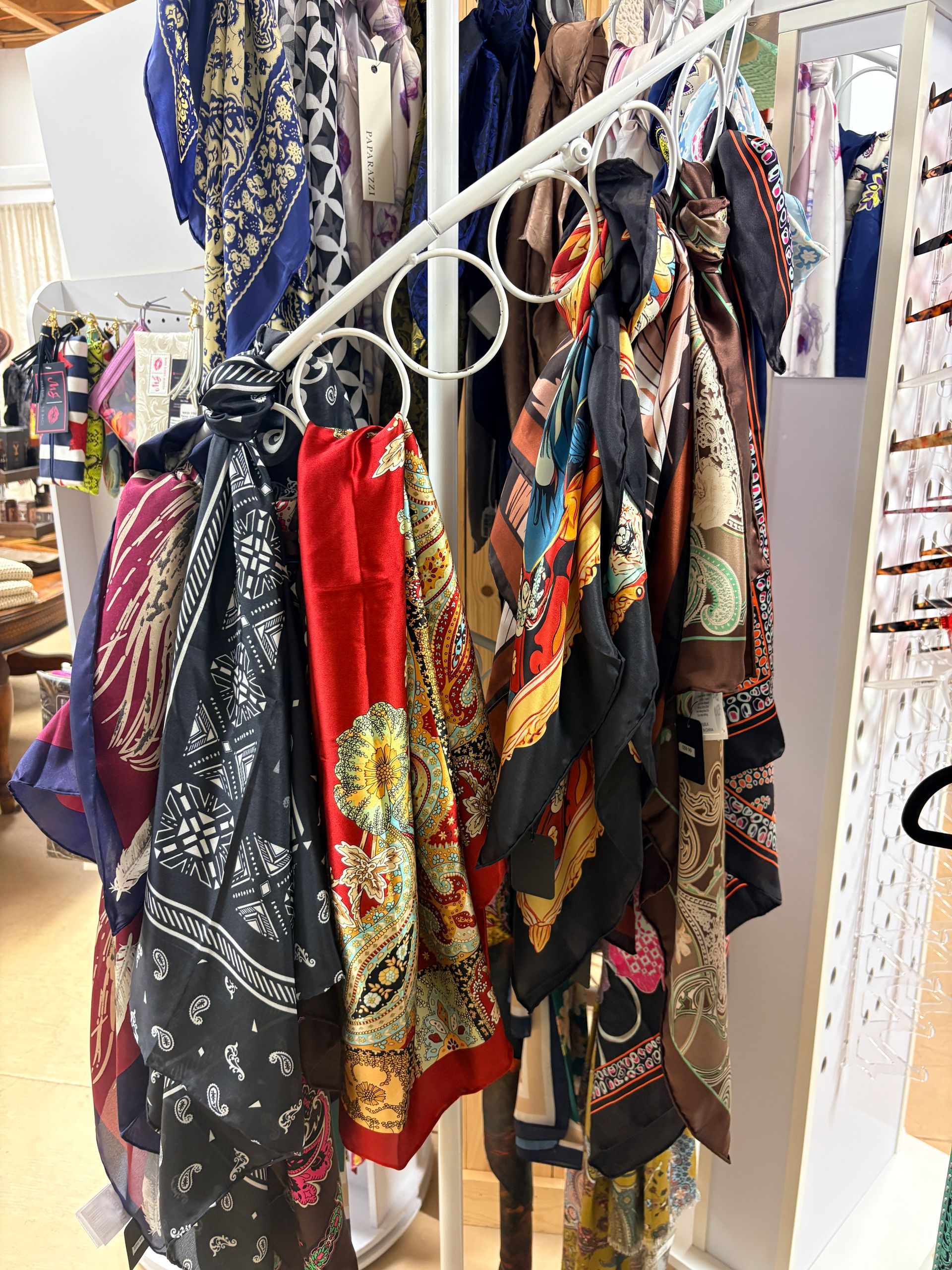 Scarves and patterned fabric wraps hanging on a white display rack in a shop