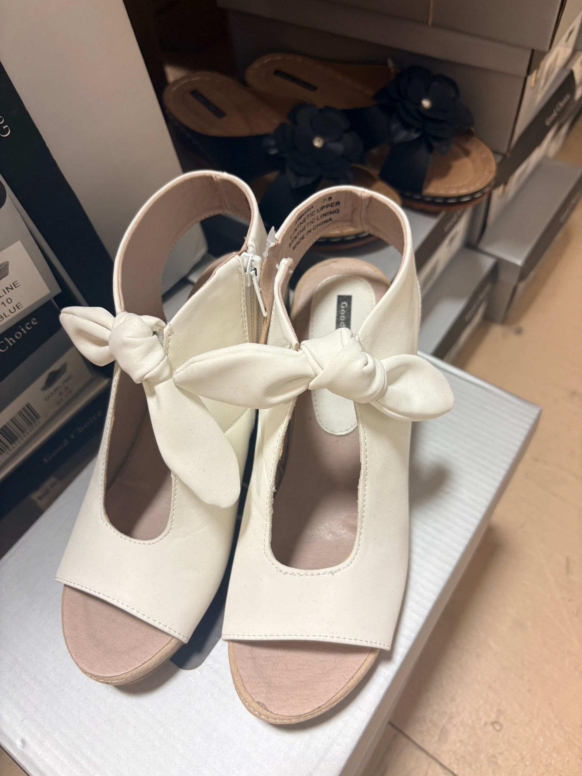 Pair of cream peep-toe heels with bow straps on a white box in a store display