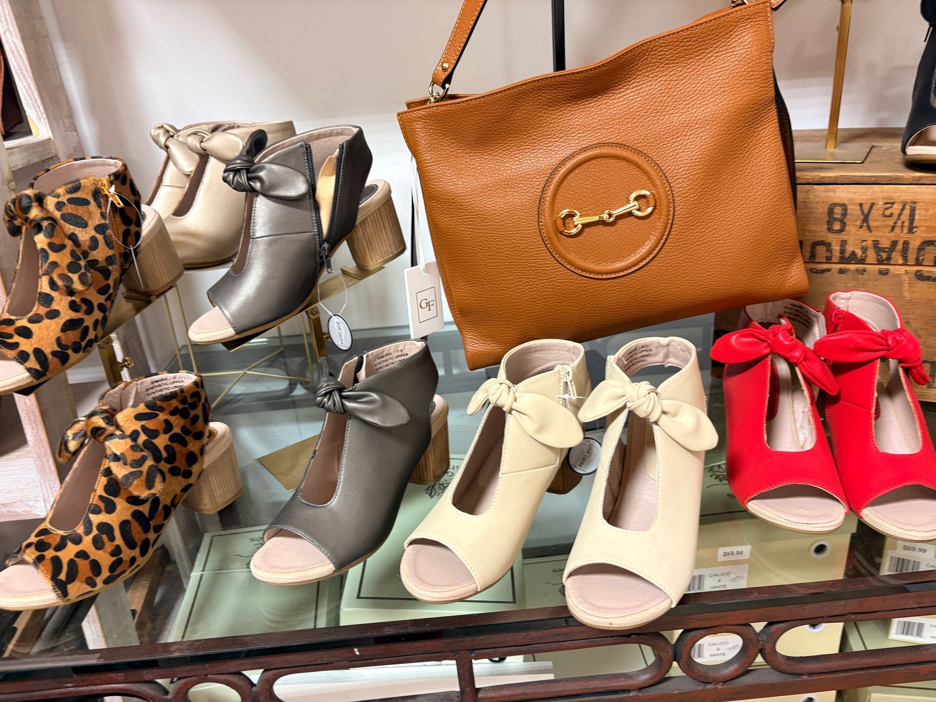 Display of women’s heeled shoes in leopard, silver, beige, and red with a tan handbag in a shop window
