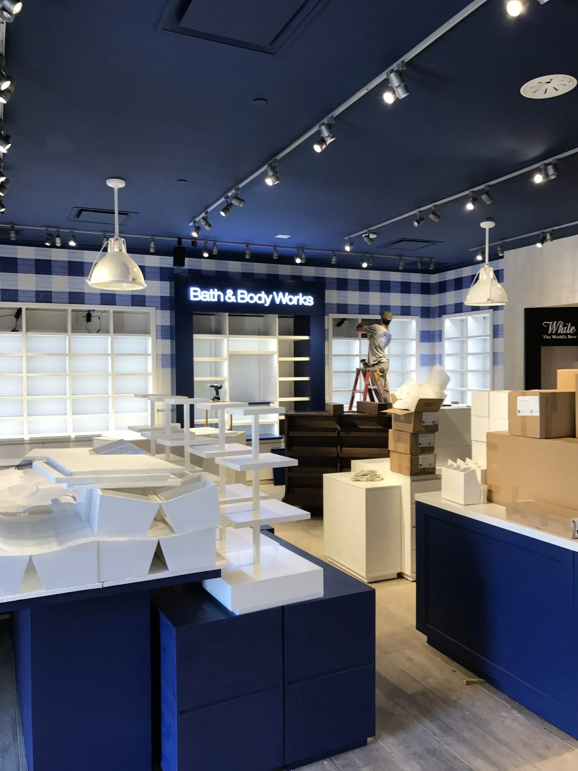 Bath & Body Works store interior with blue and white decor, shelves, and lighting; boxes and set-up underway.