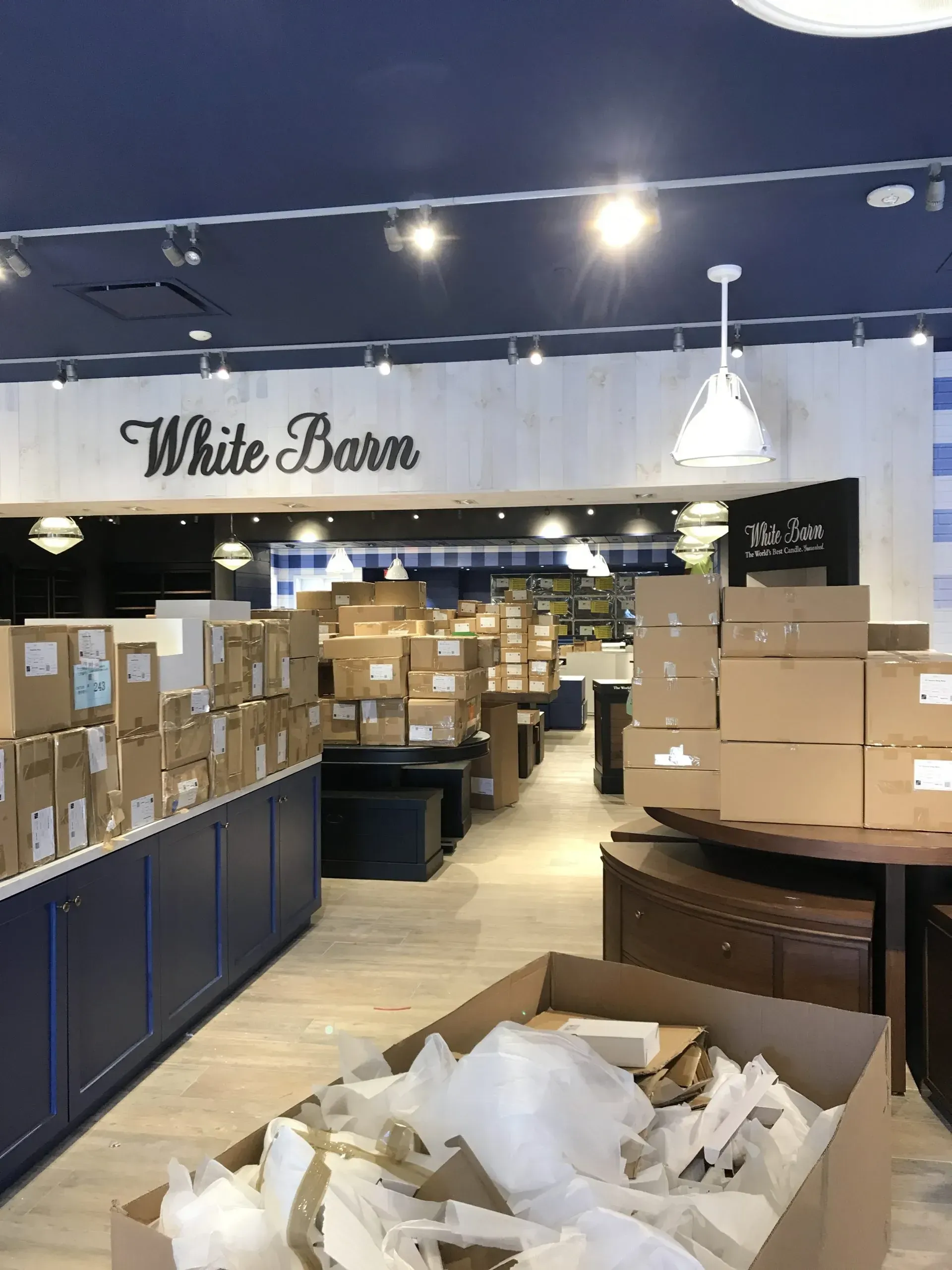 Inside a White Barn store: boxes stacked throughout, employees likely restocking shelves.