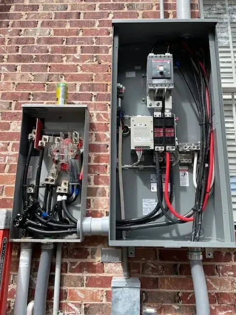 Electrical panels mounted on a brick wall, with exposed wires and breakers.