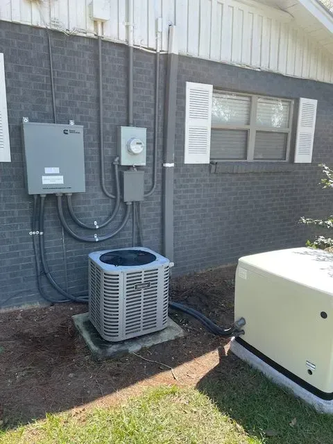 Exterior view of an air conditioning unit, electrical boxes, and a generator mounted on a brick wall.