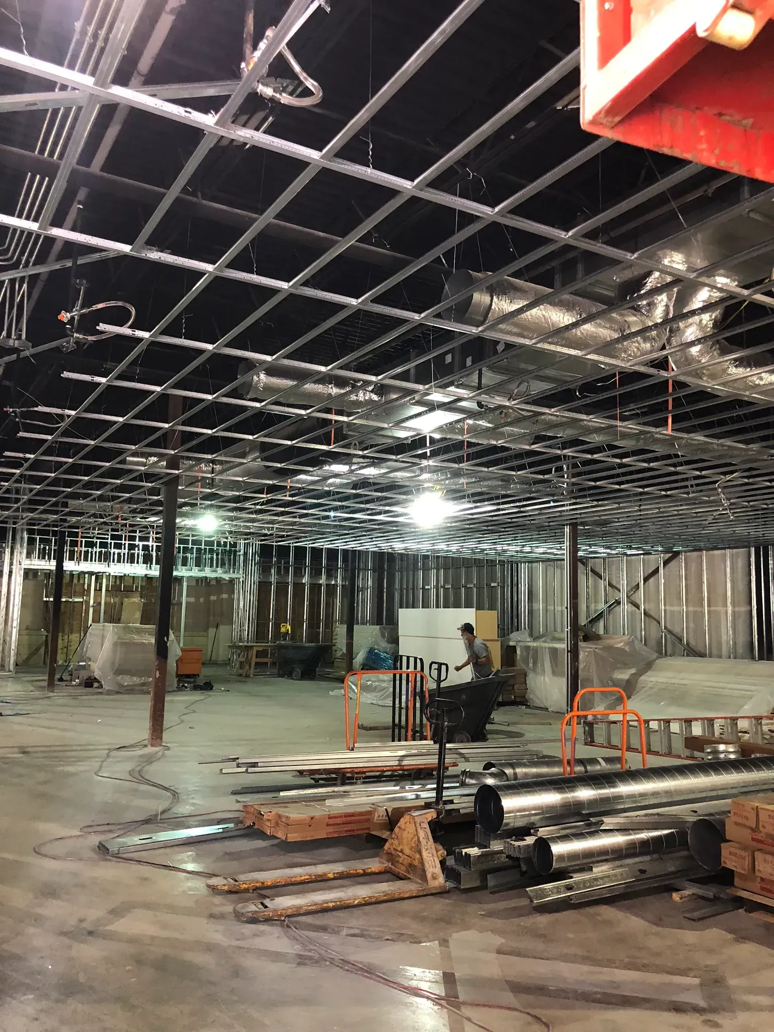 Construction site interior with exposed ceiling grid, partially framed walls, and equipment.