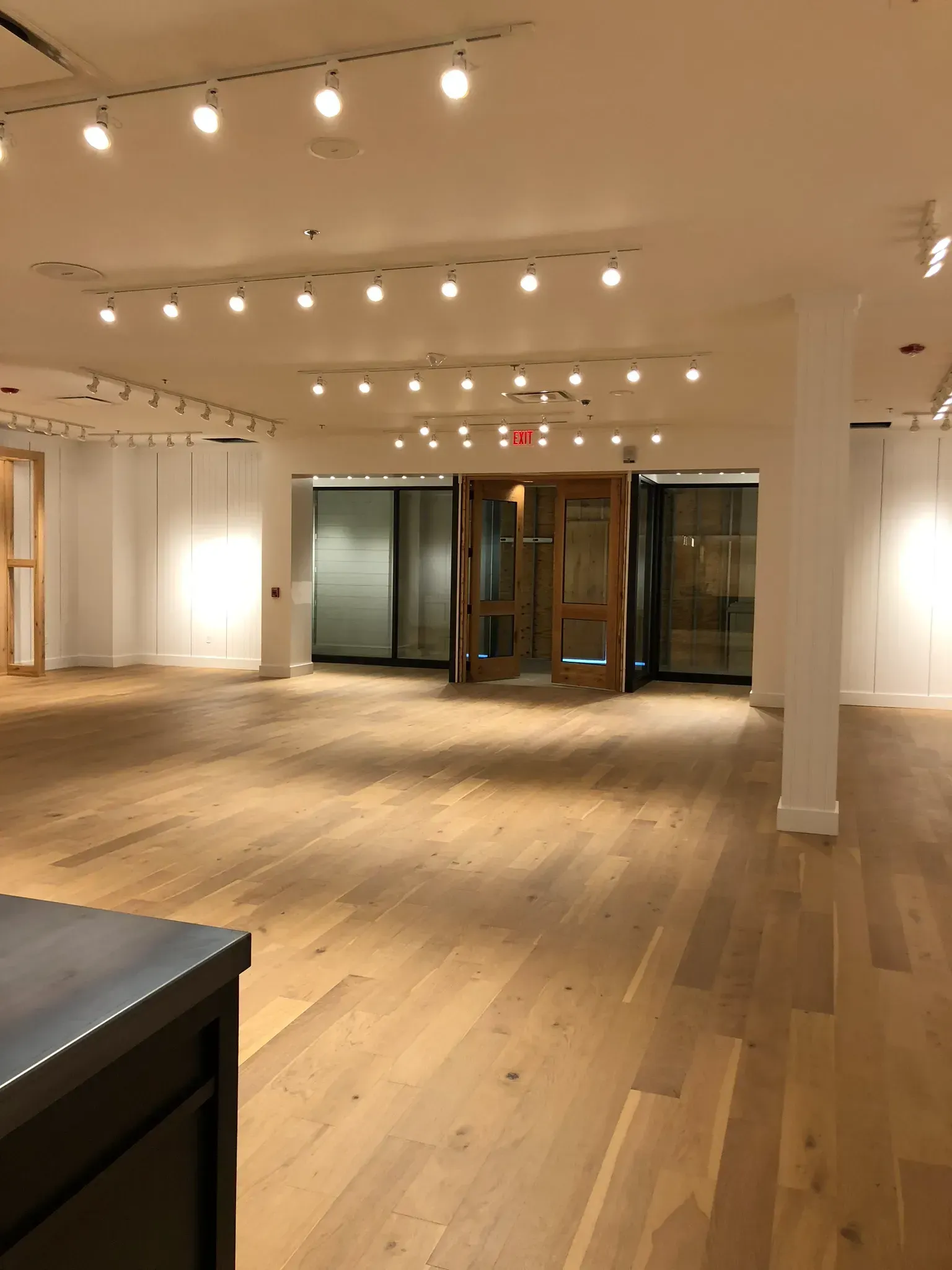 Empty retail space with hardwood floors, white walls, track lighting, and a wooden entrance door.