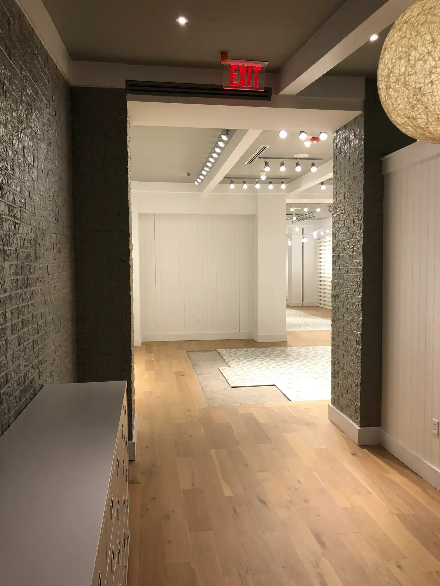 Hallway leading into a store. Gray and white walls, wood floor, decorative lighting.