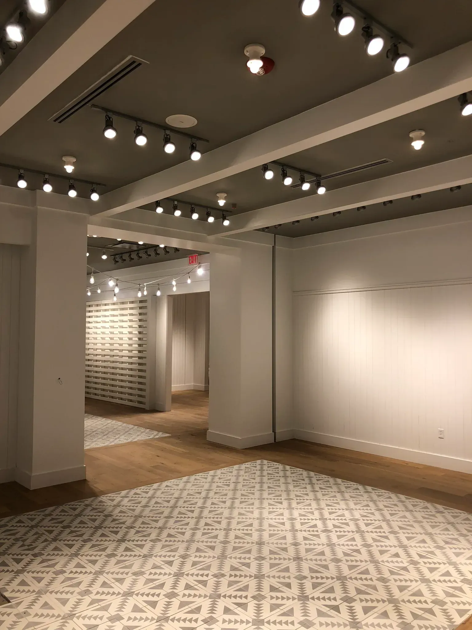 Empty interior retail space with track lighting, white walls, wood floors, and patterned tile.