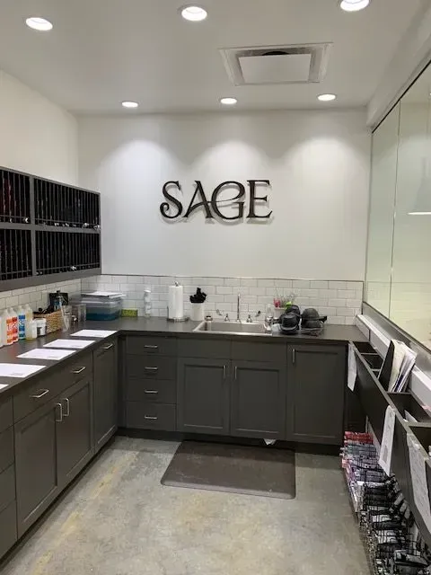 Sage salon workspace with dark gray cabinets, a stainless steel sink, and white brick backsplash.
